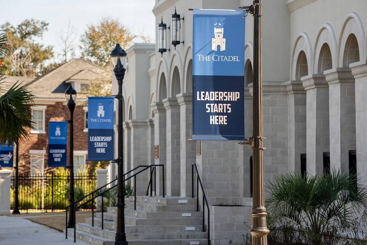 Banners reading "The Citadel: Leadership Starts Here" hang outside a building with arched windows.